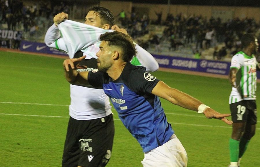 El central del San Fernando CD Carlos Blanco corre a celebrar su golazo ante la desesperación de un jugador del Atlético Sanluqueño.